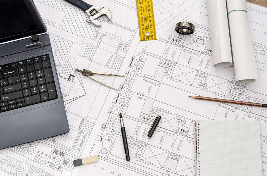 Building plans underneath a laptop and other tools representing the philosophy of general contractor Via Meridiana Contractors LLC in Westmont, IL